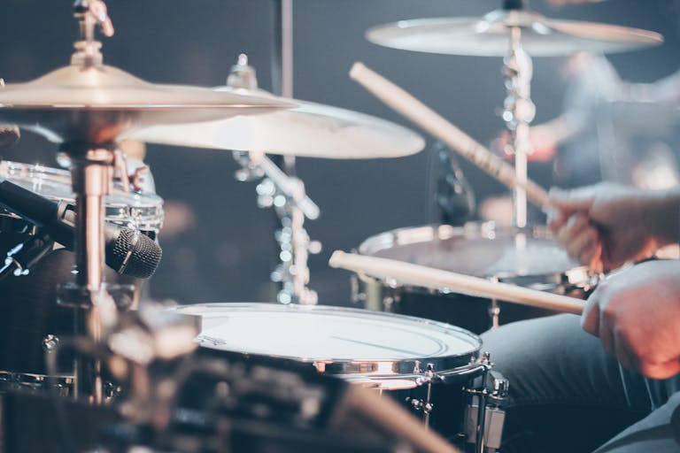 Close-up of a drummer performing on stage with focus on drum set and drumsticks.